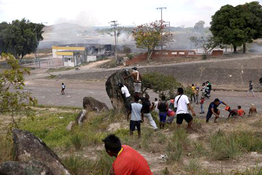 Pessoas se escondem atrás de uma rocha durante confrontos na fronteira venezuelana, em Pacaraima - Foto: REUTERS / Ricardo Moraes